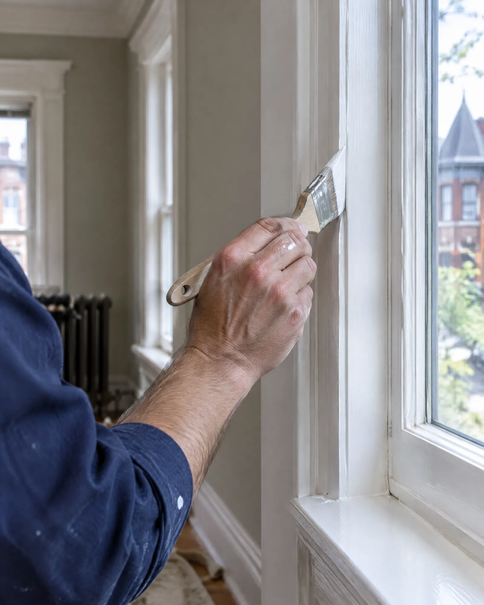 A painter’s hand cutting in a clean line along a window casing with a sash brush