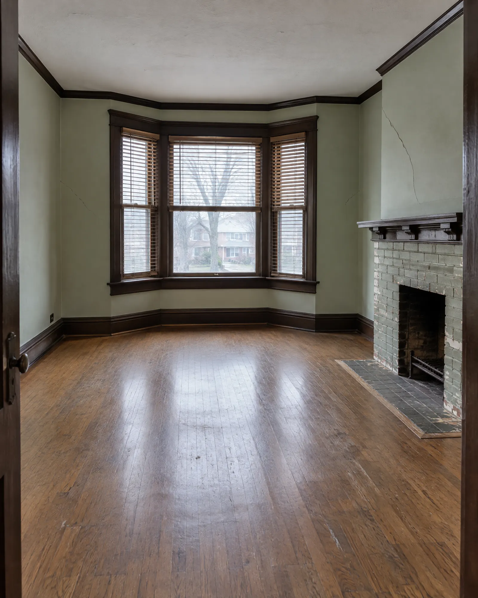 Front room of a semi-detached house, faded green walls and painted brick fireplace, before and after repainting (before)