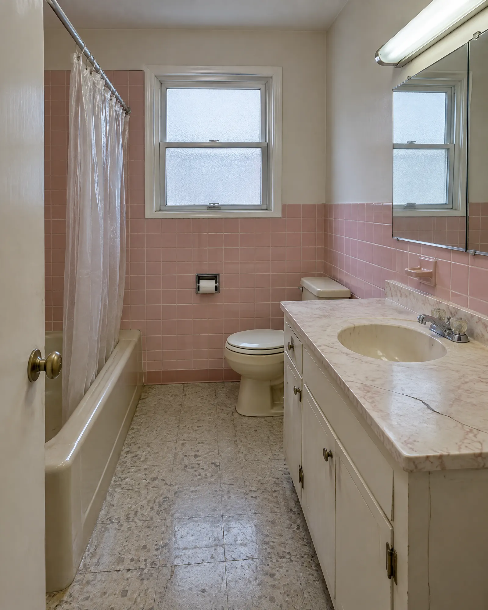 Small bathroom from the doorway, pink 1960s tile before and full renovation after (before)