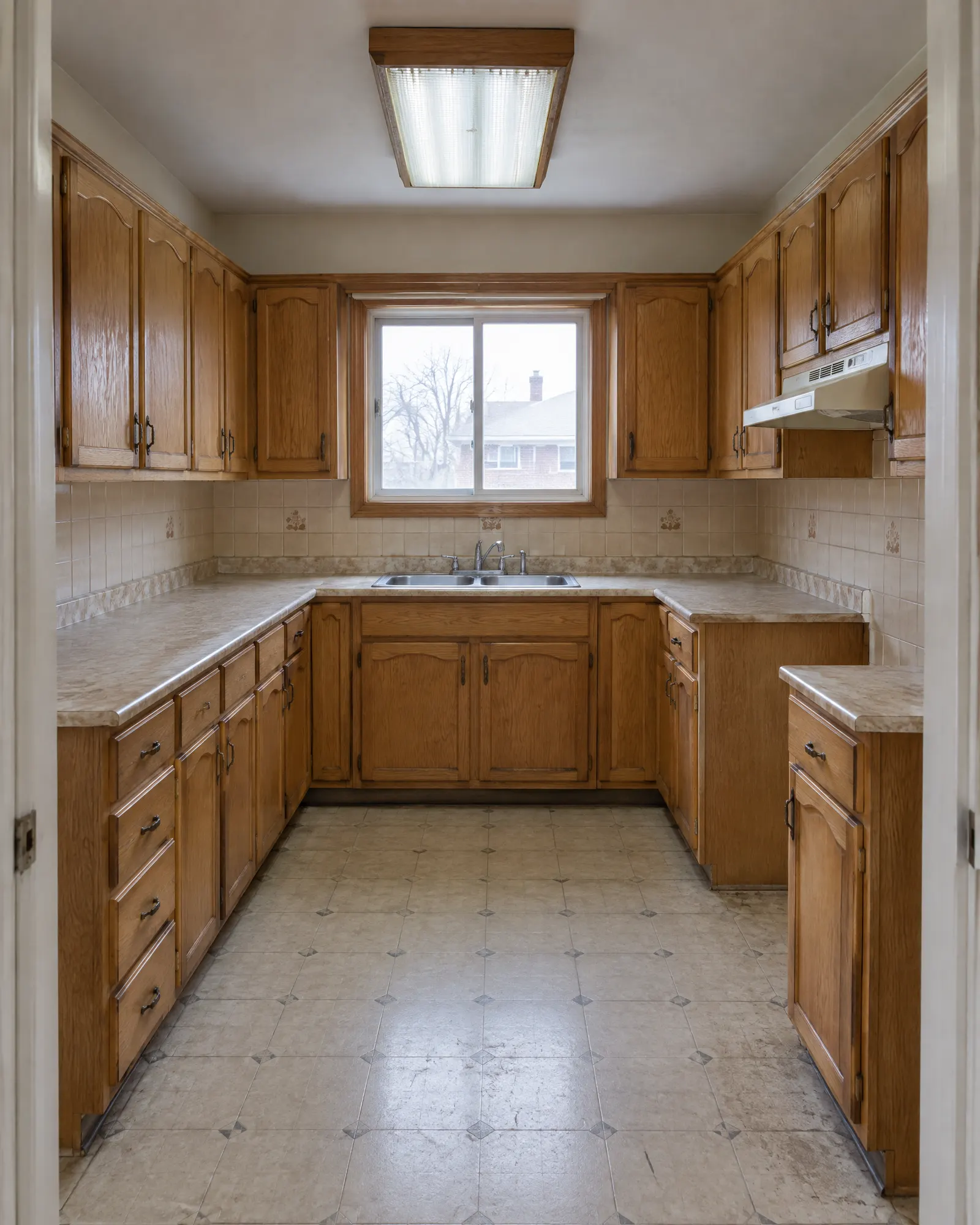 Small kitchen before renovation: dated oak cabinets, laminate counter, fluorescent light